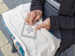 Woman lace-maker sits with needlework on knees and embroiders. Pano Lefkara, Cyprus.  