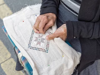Poster Woman lace-maker sits with needlework on knees and embroiders. Pano Lefkara, Cyprus.   © shujaa_777