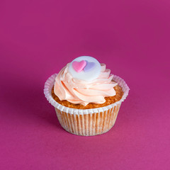 Cupcake for Valentine's Day with hearts on top of whipped cream on colourful background.