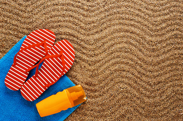 Flip-flops, sunscreen spray and towel on the beach.