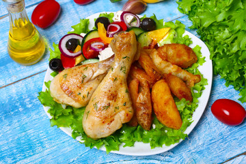 roasted chicken legs with potatoes with Greek salad on wooden background with vegetables