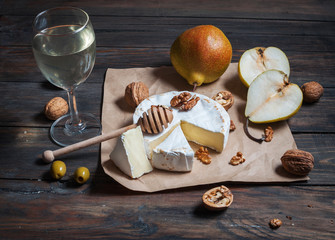 Camembert cheese with walnuts, honey and pears on rustic table. Glass of white wine