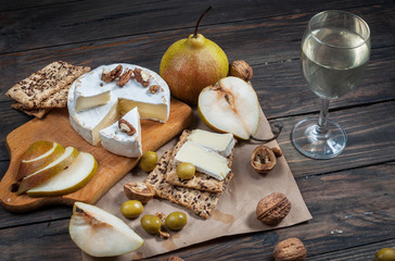 Camembert cheese with walnuts, honey and pears on rustic table. Glass of white wine
