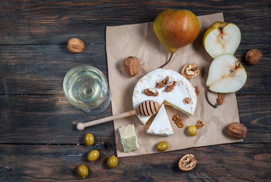 Camembert cheese with walnuts, honey and pears on rustic table. Glass of white wine