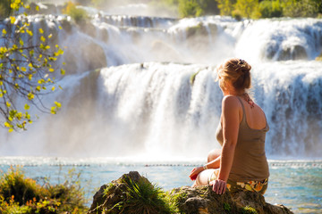 Lovely young woman sitting at a waterfall in Krka national park