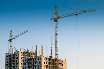 two construction cranes and skyscraper under construction