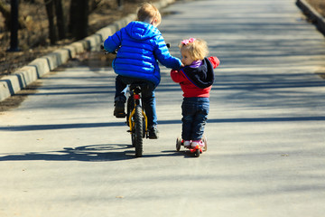 little boy on bike teaching baby girl to ride scooter