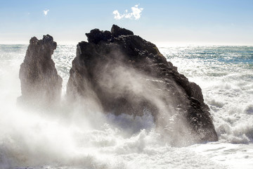 waves crashing against big rocks to the beach