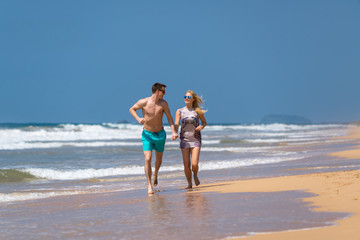 Couple Running Through Waves On Beach Holiday