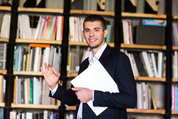 Student in library. Handsome young man holding books and smiling while standing in library