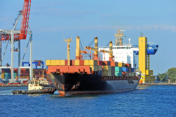 Tugboat assisting container cargo ship to harbor quayside