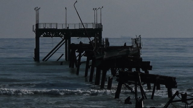 Slow motion loop waves breaking into old ruined oil rig seagulls flying by stock