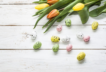 Easter background with colorful eggs and yellow and orange tulips on white wooden background