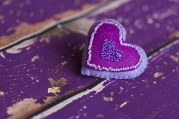 Сердечко из сиреневого/фиолетового фетра ручной работы, вышитое бисером, на старом/вытертом  деревянном полу  - obrazy, fototapety, plakaty
