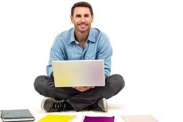 Young man sitting on floor using laptop with notepads on floor