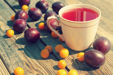 Plum compote in a white mug and fresh plums with a cherry plum on a wooden surface.