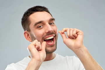 man with dental floss cleaning teeth over gray