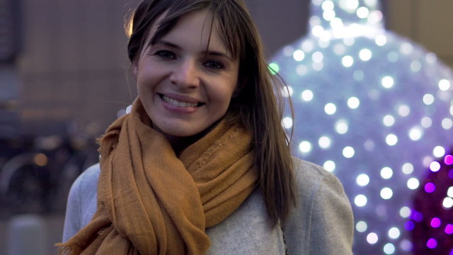 Portrait of young, happy woman sitting in the city during winter night 
