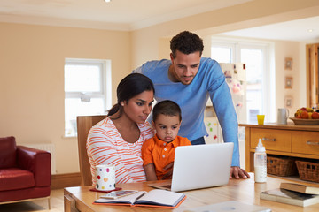 Family In Kitchen Looking At Laptop Together