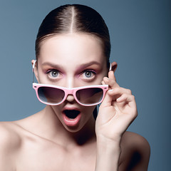 Portrait of beautiful young girl in sunglasses on a blue background, a look of surprise