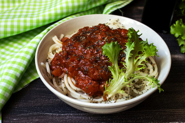 Portion of spaghetti with tomato sauce and cotton green plaid towel in brown wooden background