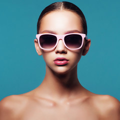 Portrait of beautiful young girl in sunglasses in studio on a blue background