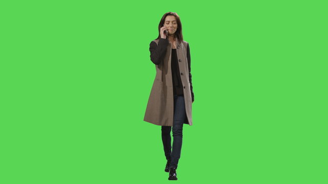 Casual young brunette girl in a dress is walking on a mock-up green screen in the background. Shot on RED Cinema Camera.