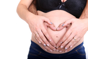hands of pregnant woman and her husband in heart shape on her be