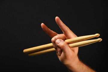 Man hand with drumsticks and devil horns over black