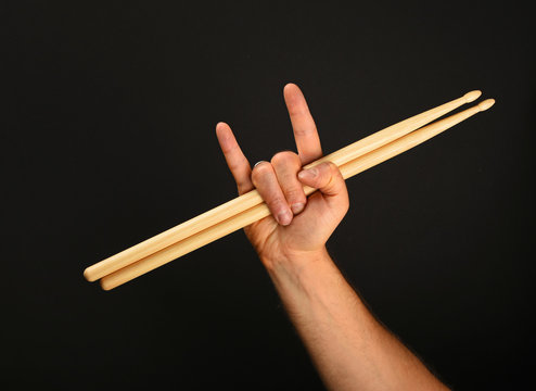 Man hand with drumsticks and devil horns over black