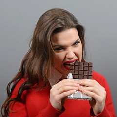 Beautiful woman eating chocolate against gray background