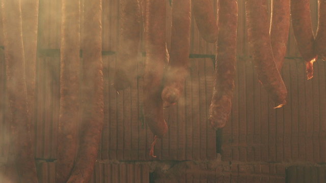 Homemade smoked sausages, cured pork meat, food preparation process in smokehouse.