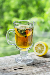 Tea with lemon and mint in glass cup on wooden rustic table in front of the window on a sunny summer day