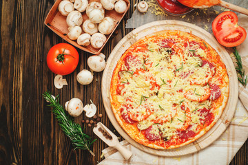 
thin-crust pizza with sausage , mushrooms, cheese , tomato sauce , rosemary and spices on a wooden background   
