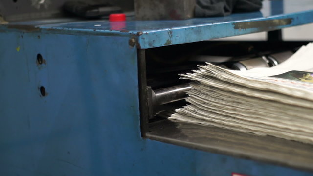 Newspapers coming off the production line at an industrial scale offset printing press and being stacked for delivery.