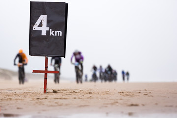 a distance sign which says that mountain bike race participants are four kilometer away from the finish during a beach biking race.
