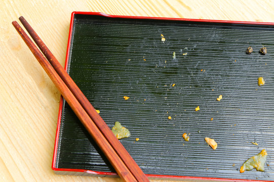 Dirty black plate with chopsticks on wooden table