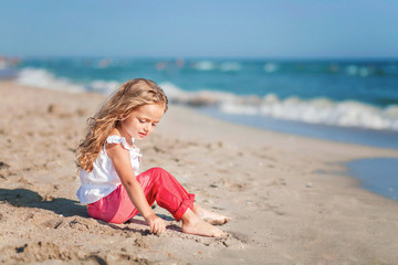 Fototapeta na wymiar little girl sitting on the beach in pink pants