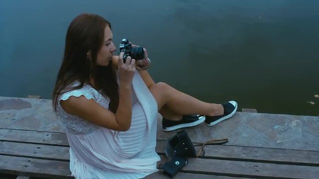 Young attractive Caucasian woman taking pictures with vintage camera on an old pier. Canon RAW edited footage