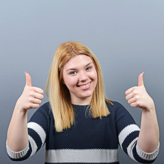 Portrait of happy woman holding thumbs up against gray backgroun