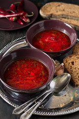 Two bowls with traditional Ukrainian vegetable borscht on the black wooden background