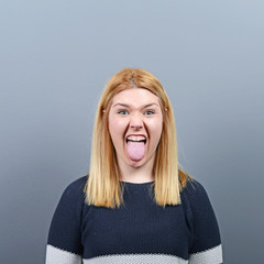 Portrait of woman sticking out her tongue against gray backgroun