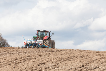 Fototapeta premium Agricultural drill or planter on a hilltop skyline planting the spring crop with ploughed earth texture in the foreground