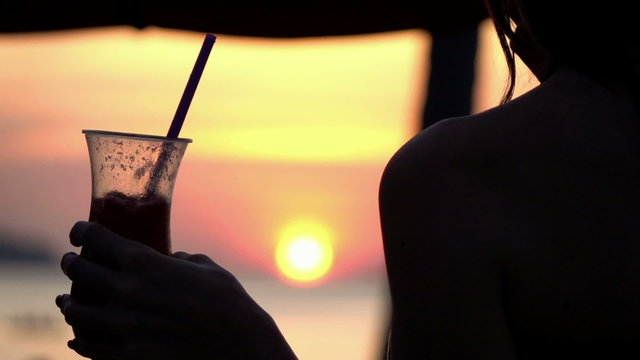 Silhouette of woman holding cocktail on sunbed during sunset, slow motion 240fps
