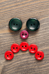 Sad face made of colored buttons on wooden table
