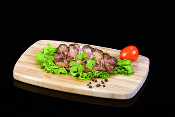 Tasty grilled ribs with a parsley on top, lettuce leaf and a tomato on a wooden breadboard