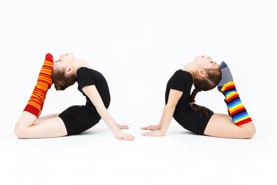 Two flexible teen girls doing gymnastics exercises on a white ba