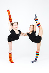 Two flexible teen girls doing gymnastics exercises on a white ba