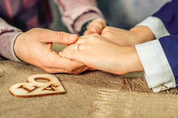 Man's hands are giving little wooden heart to woman's hand. Couple gives each other a hand