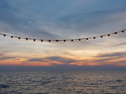 Fototapeta light bulbs on string wire against sunset sky by the beach